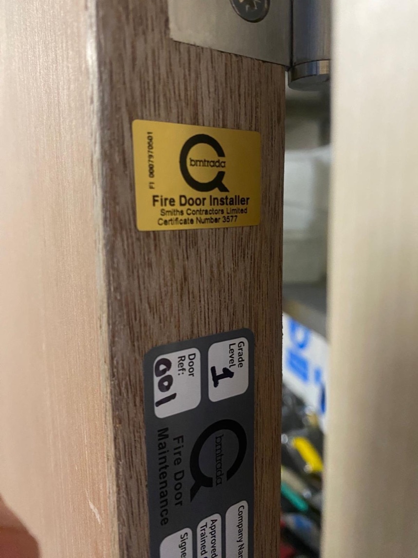 BM TRADA Q-Mark fire door installer label fixed to the edge of a door leaf